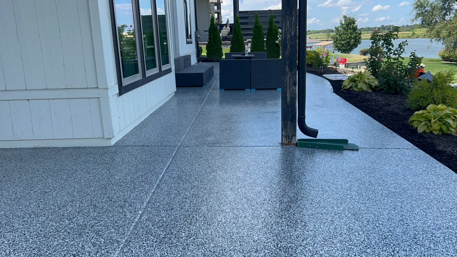 Lengthwise view of a finished patio floor coating beside a white home with a lake in the distance